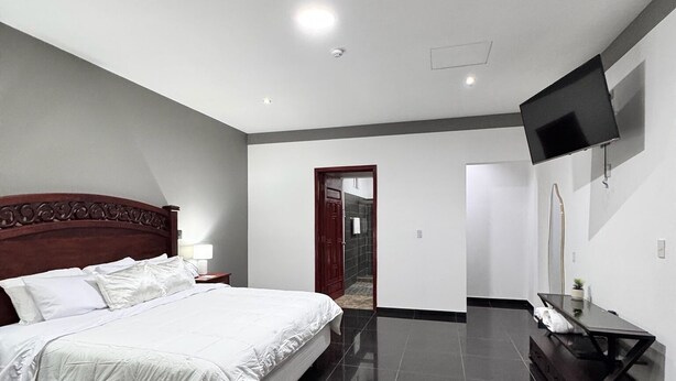 Une chambre à coucher moderne avec un grand lit, un téléviseur à écran plat fixé au mur et une tête de lit en bois foncé.