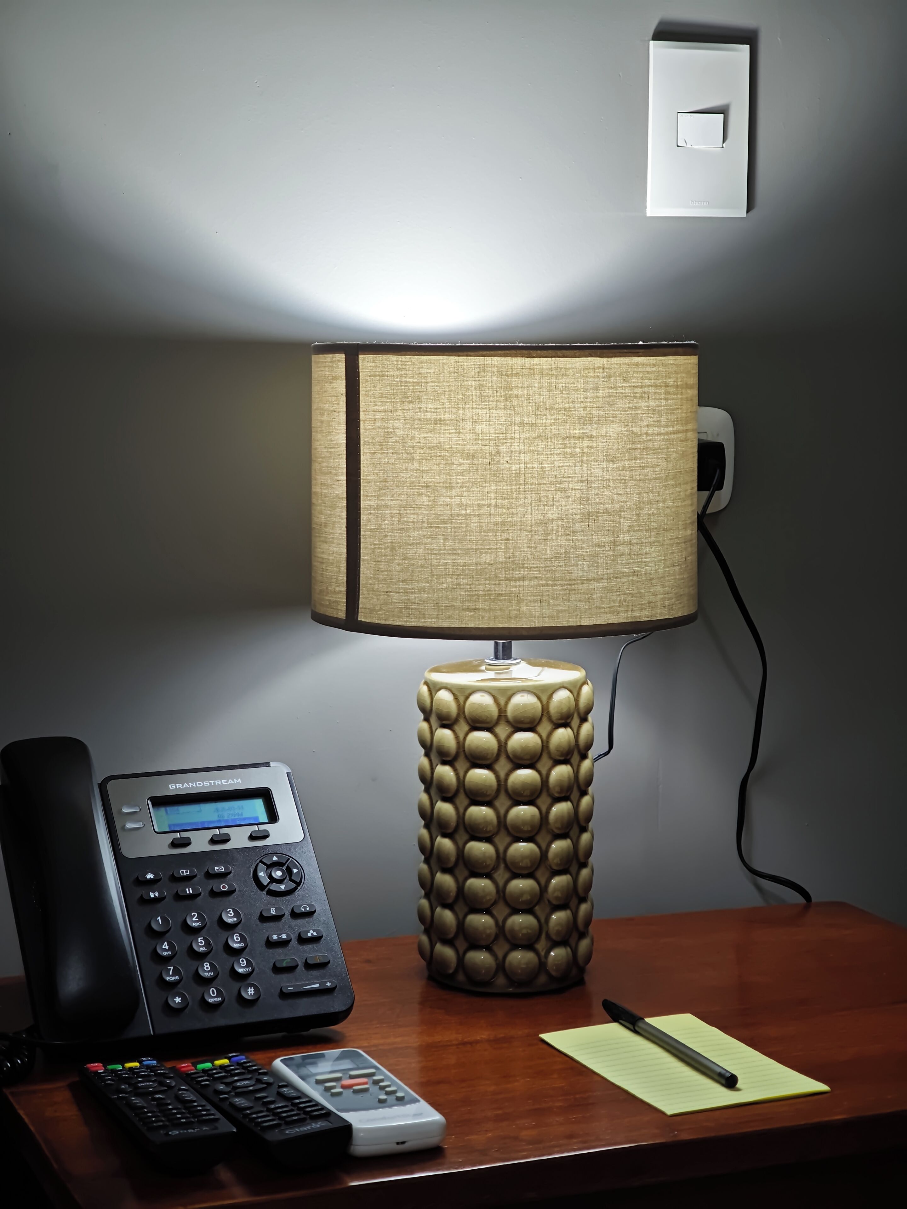 A desk with a telephone, a lamp, and a remote control.