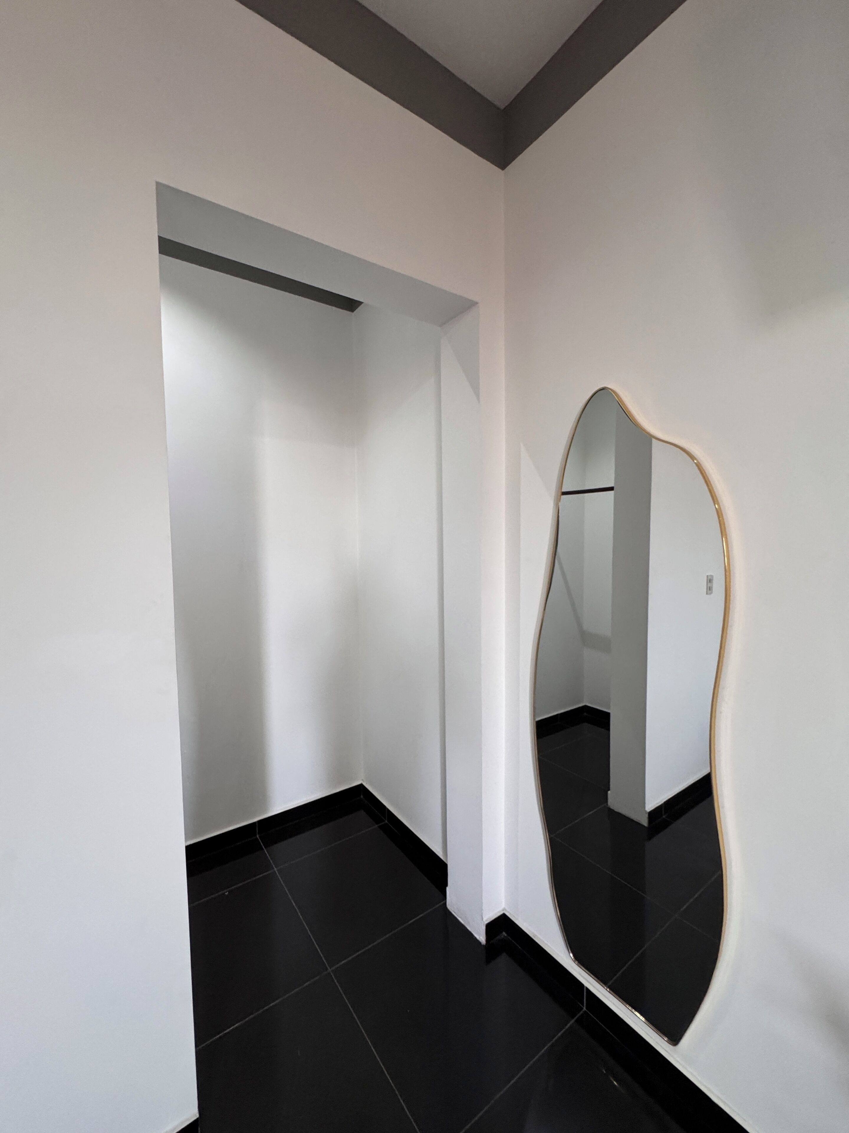Een kamer met een grote spiegel, een vloer van zwarte tegels en witte muren.