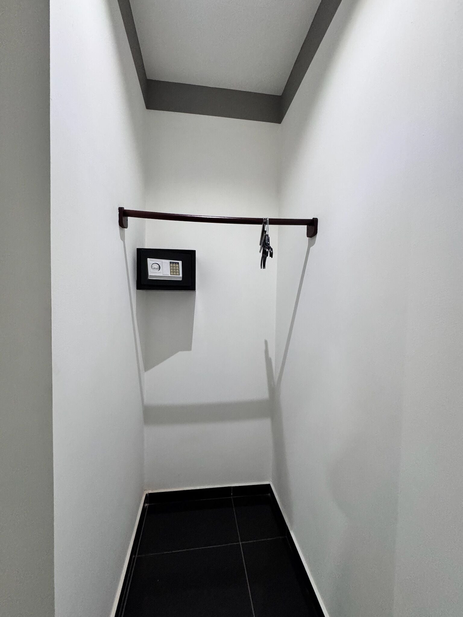 Une petite pièce étroite, dotée d’un sol carrelé de carreaux noirs, d’un mur blanc et d’un plafond avec des moulures sombres.