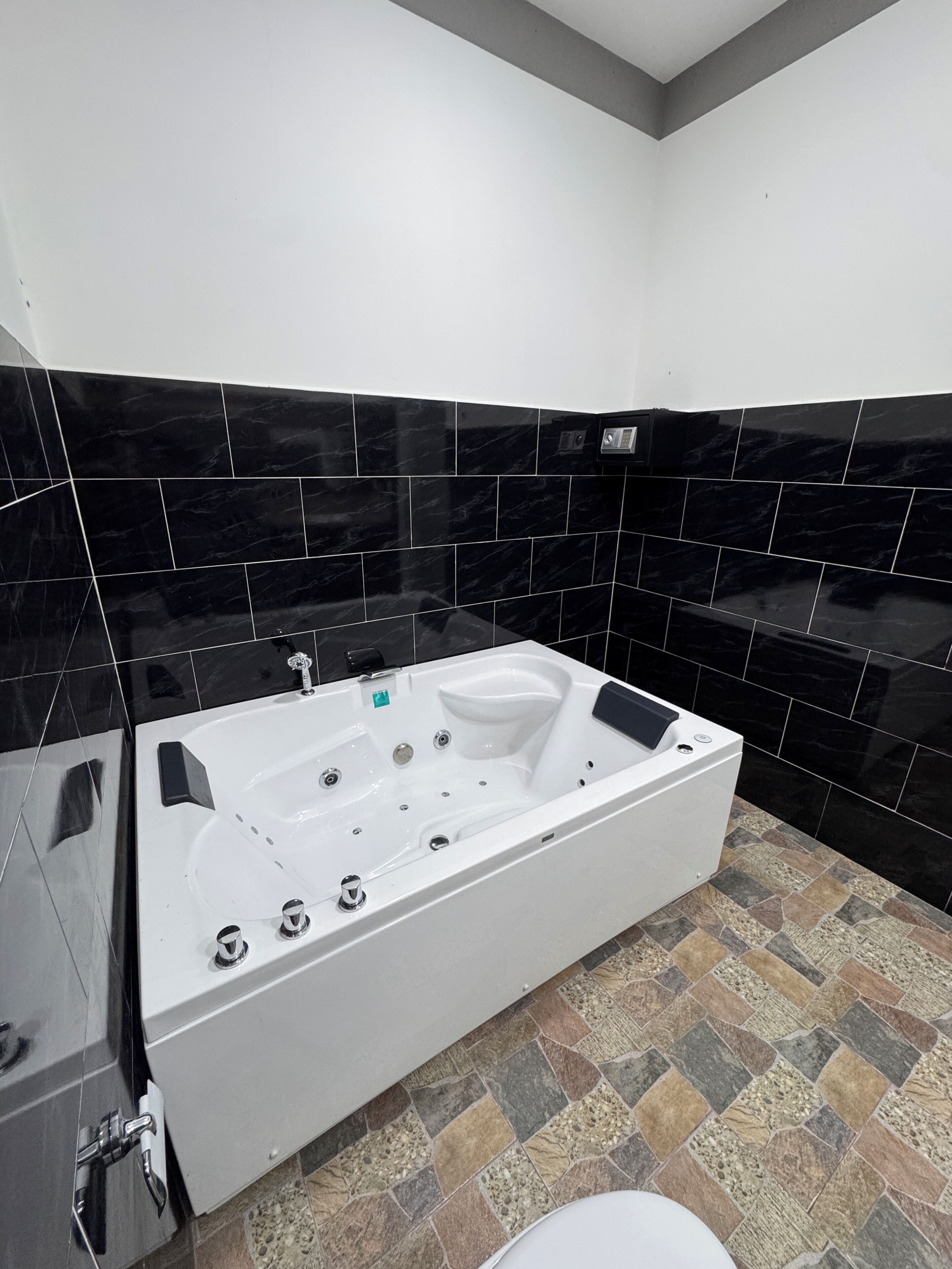 Un baño moderno con una bañera blanca grande, paredes de azulejos negros y un piso con diseño de piedra.