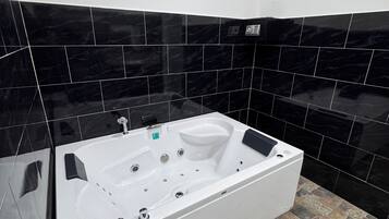 Un baño moderno con una bañera blanca grande, paredes de azulejos negros y un piso con diseño de piedra.