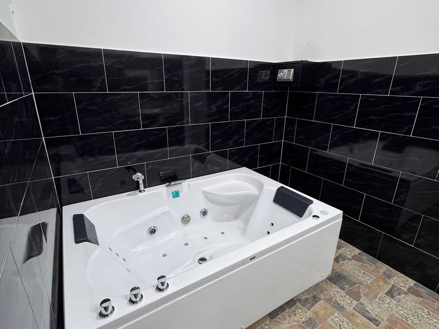 Un baño moderno con una bañera blanca grande, paredes de azulejos negros y un piso con diseño de piedra.