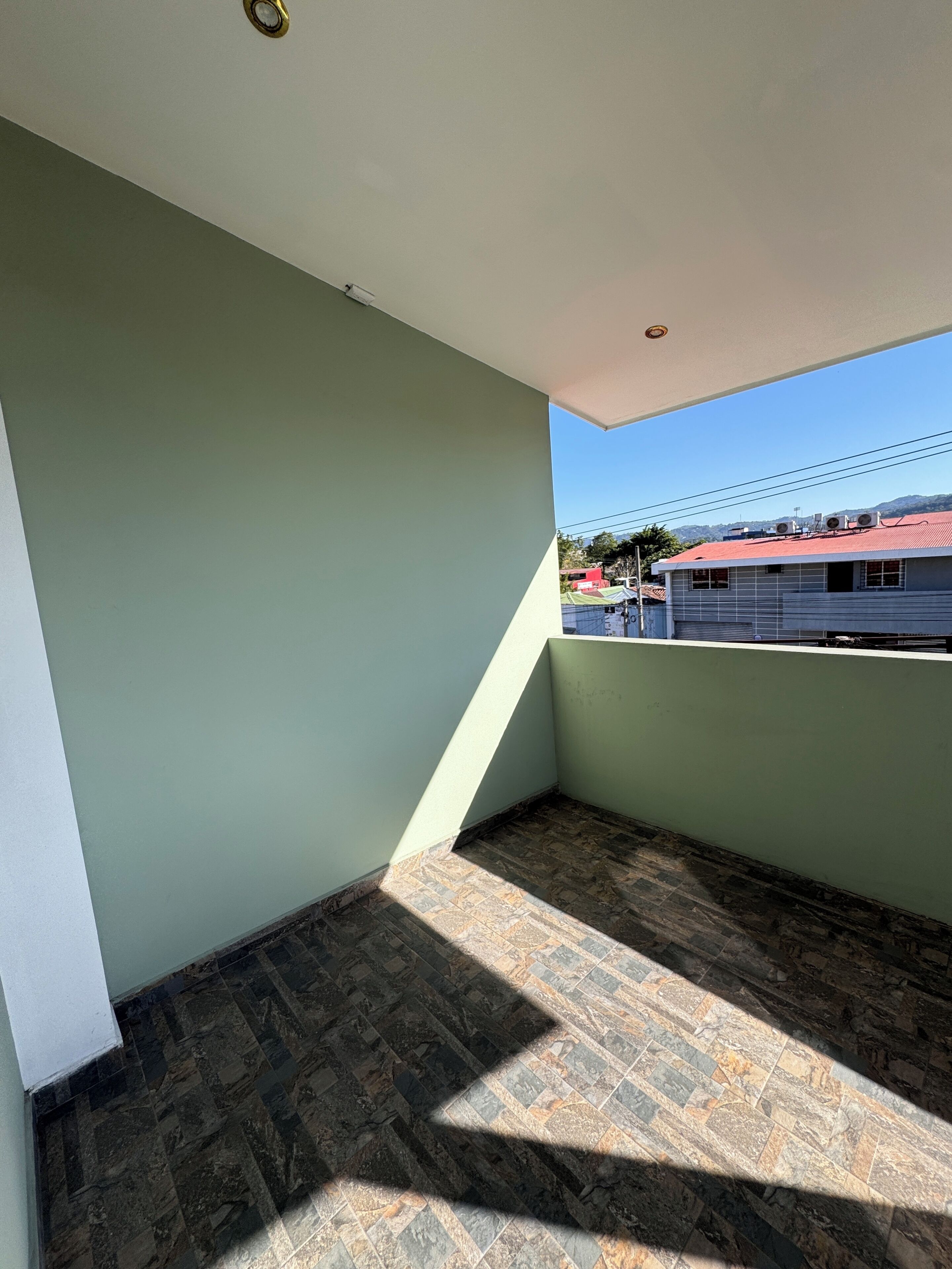 Une pièce avec un plafond en pente, une vue sur un bâtiment à toit rouge et un sol à motifs.