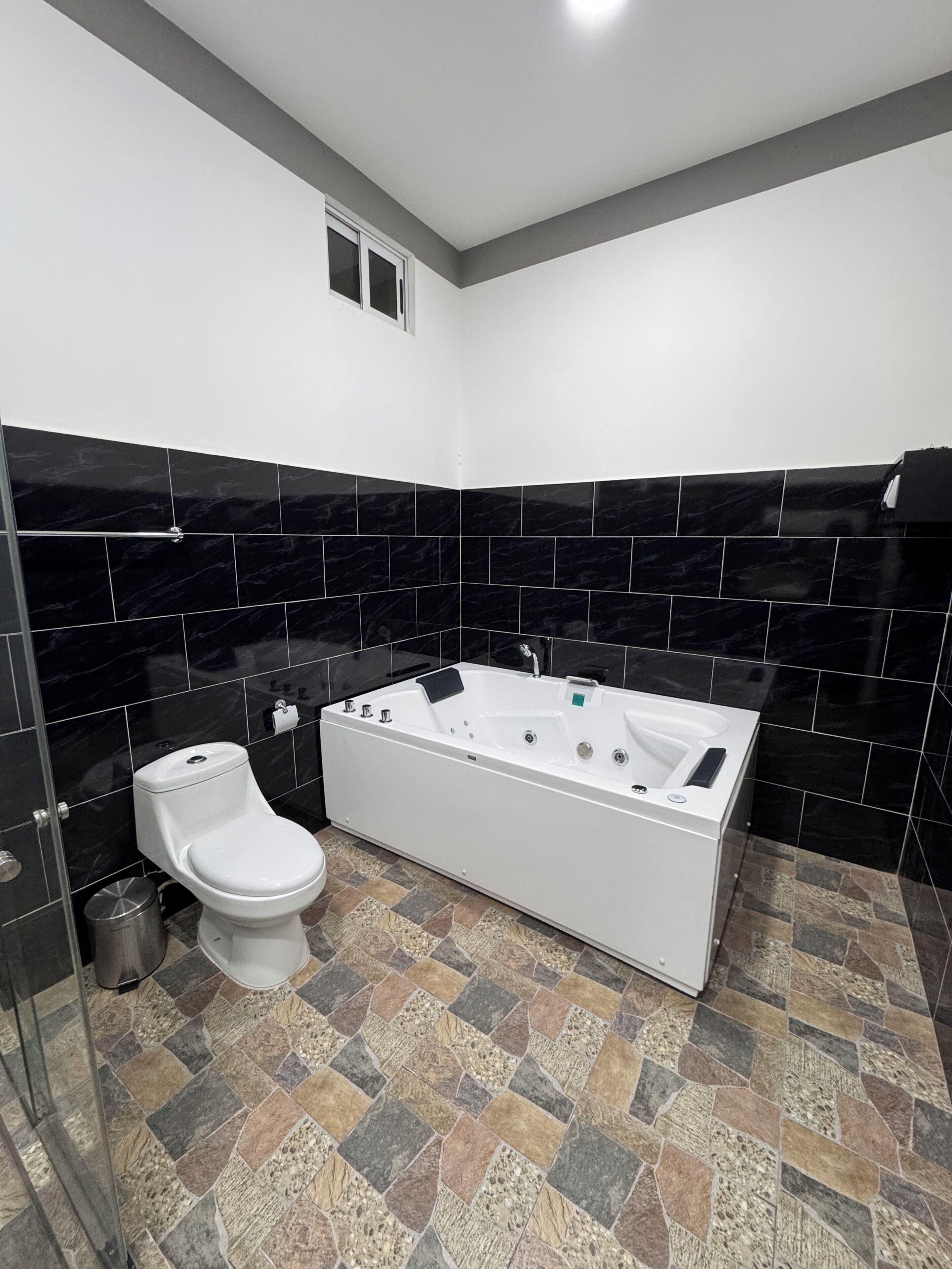 A modern bathroom with a white bathtub, a toilet, and black marble tiles.