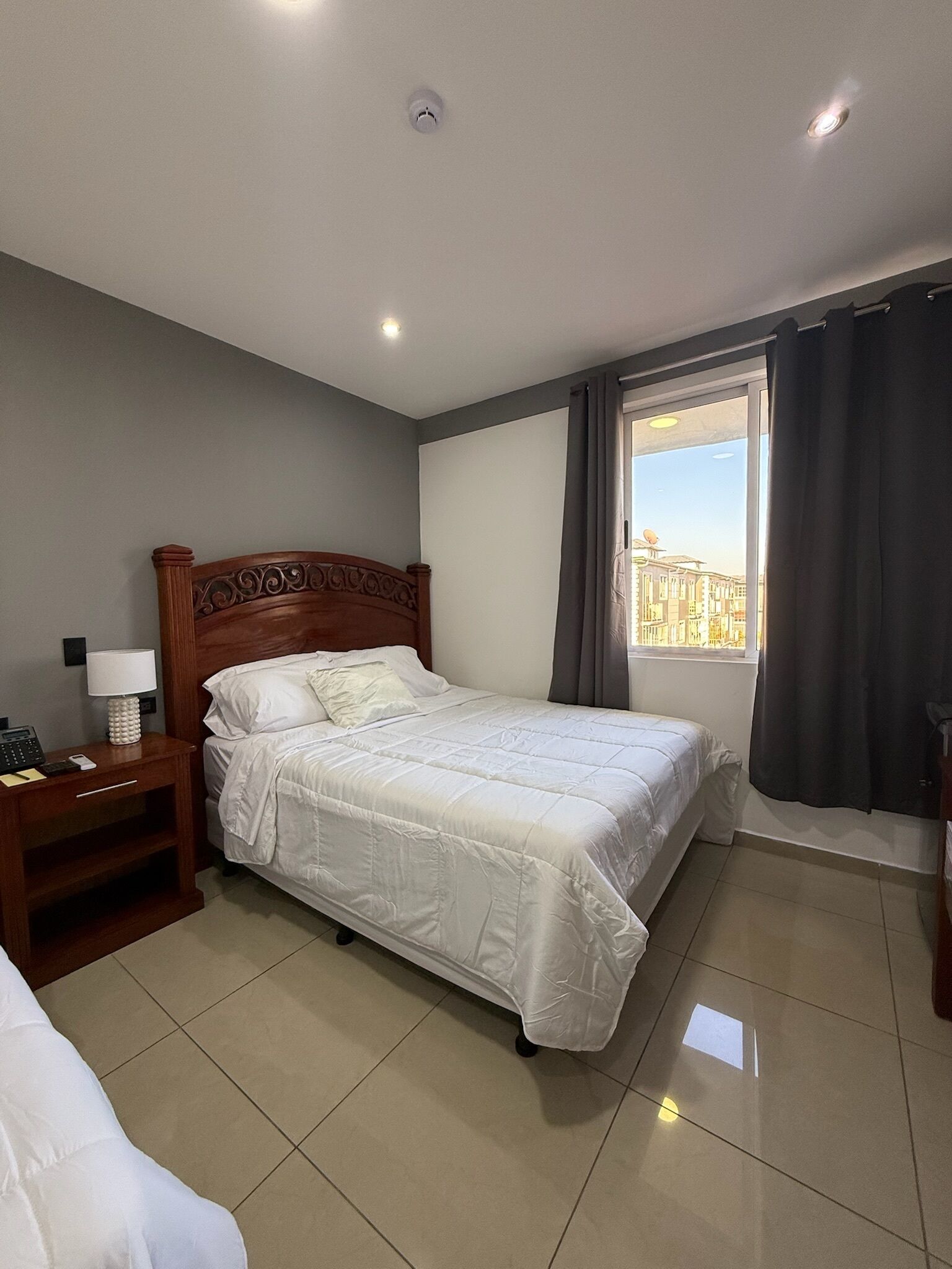 A hotel room with a bed, bedside table, lamp, and a window with curtains.