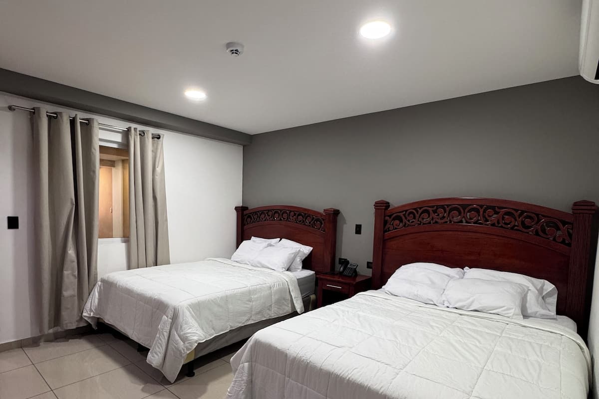 Habitación de hotel con dos camas, un baño y una pequeña mesa.