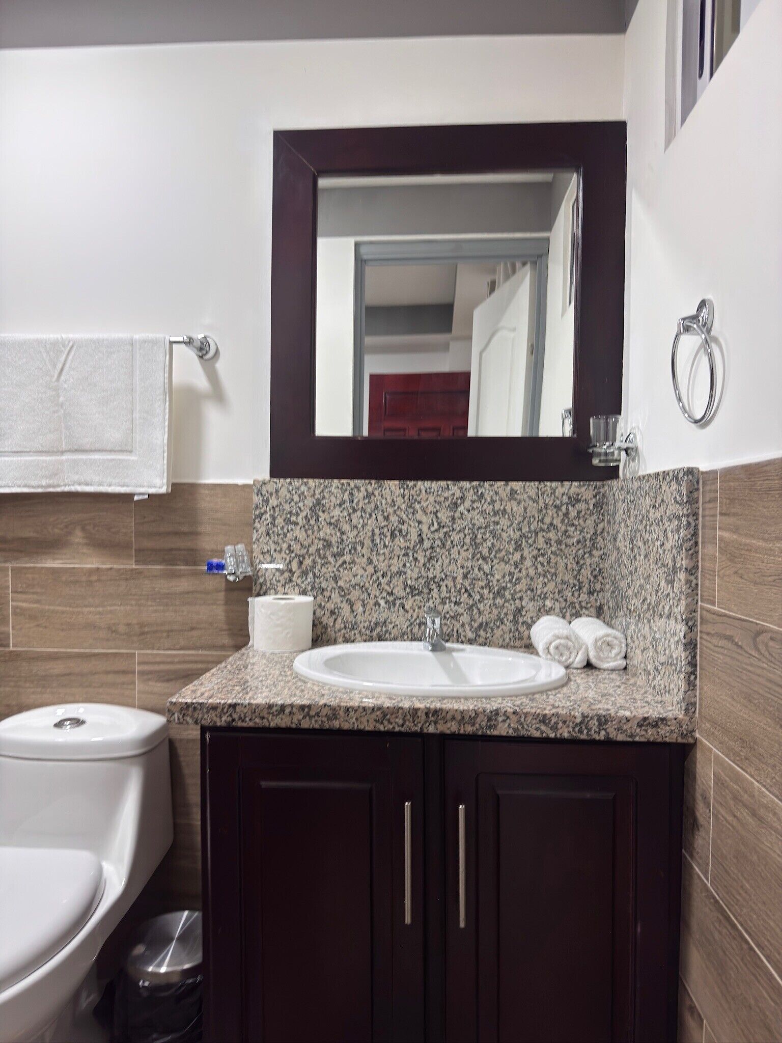 Une salle de bain avec un lavabo blanc, des meubles en bois foncé, un plan de toilette en marbre, des toilettes et un miroir au-dessus du lavabo.