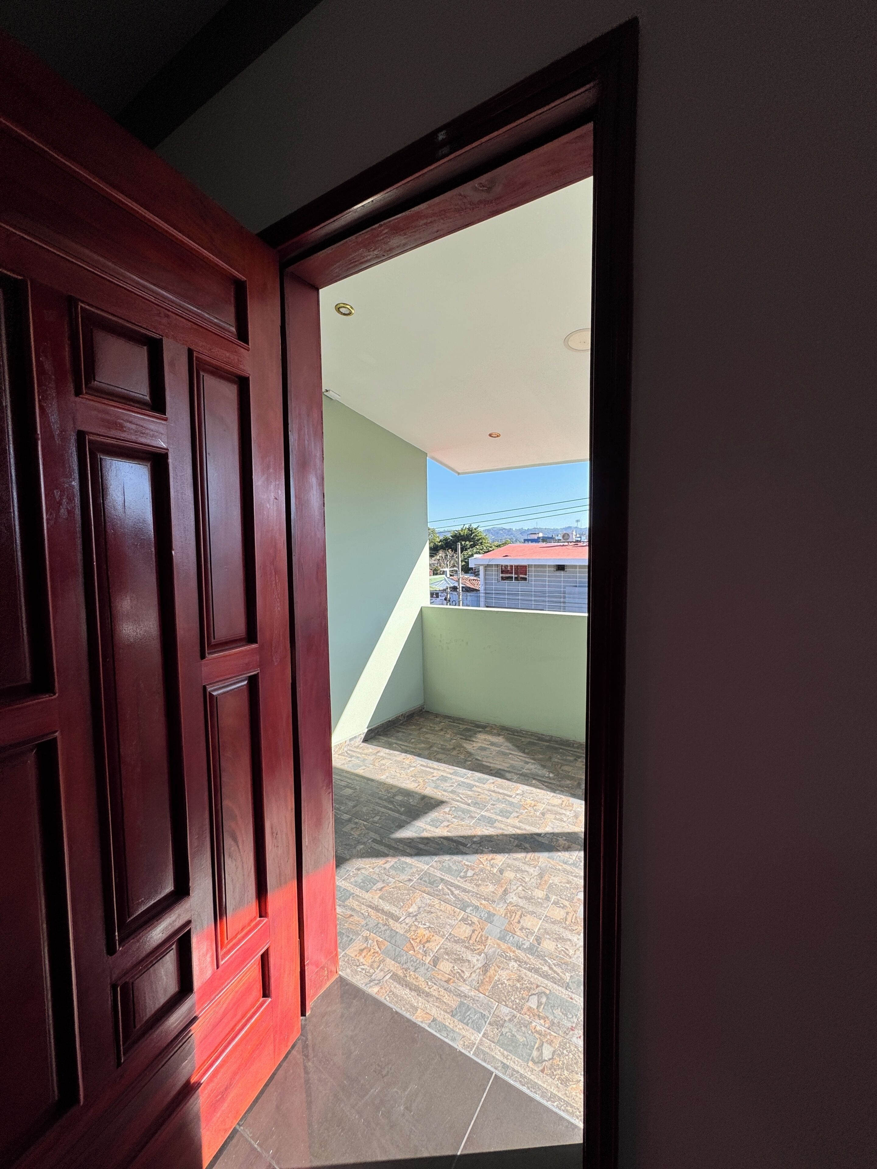 A doorway leading to a balcony with a tiled floor and a view of a building in the distance.