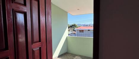 A doorway leading to a balcony with a tiled floor and a view of a building in the distance.
