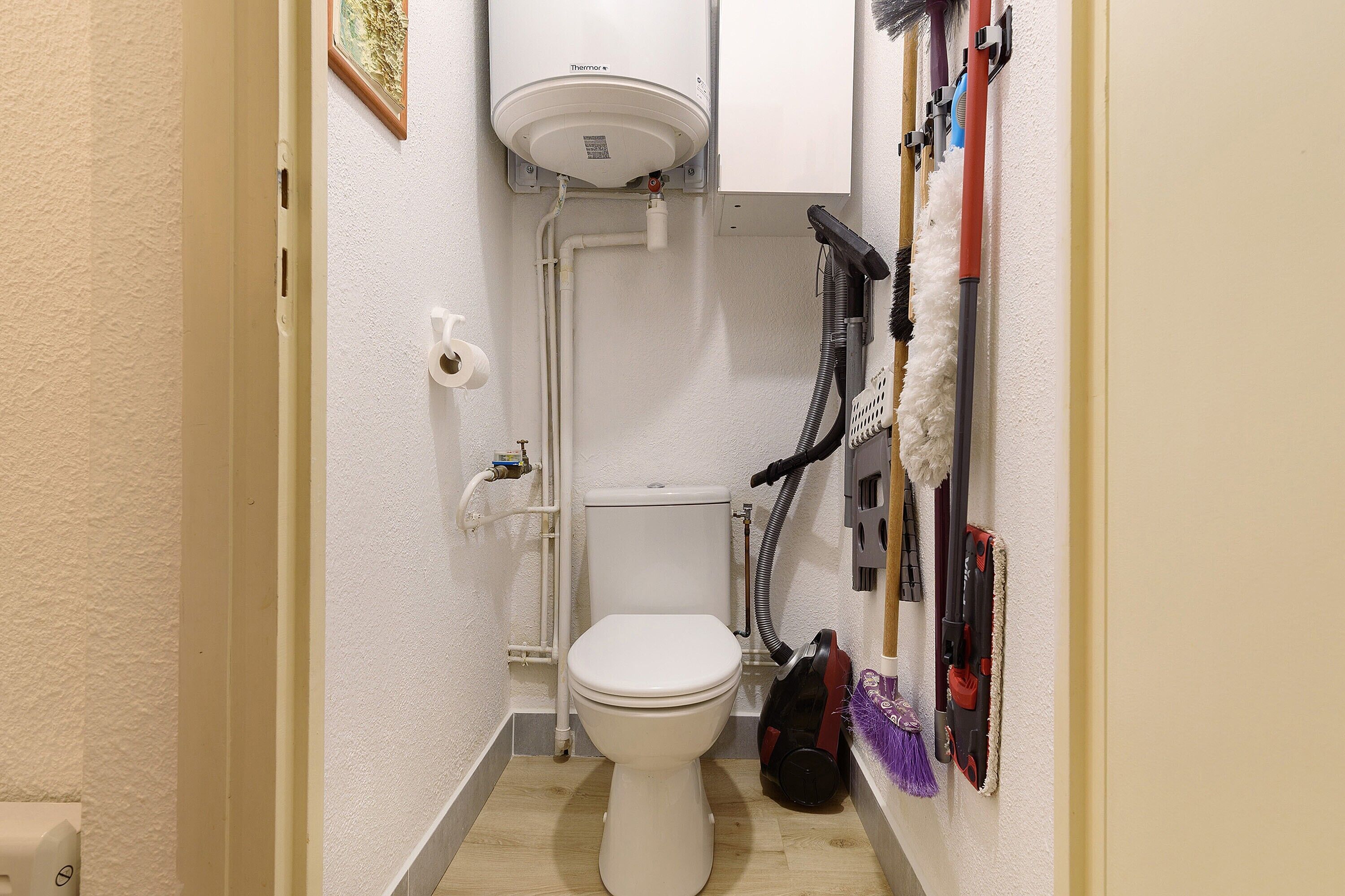 Un bagno piccolo e compatto con il water, un riscaldatore a muro bianco e un aspirapolvere a muro.