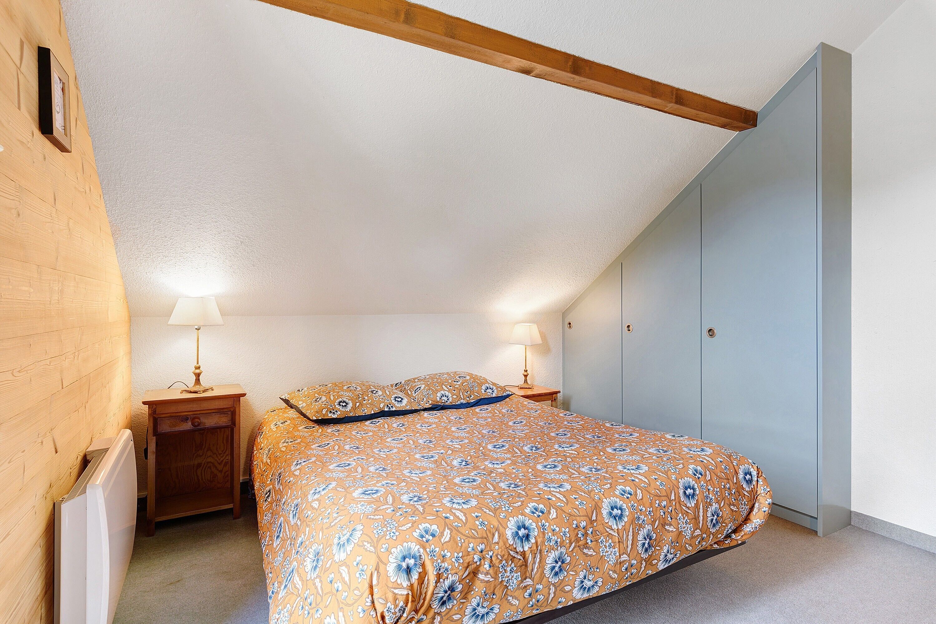 A bedroom with a bed, two bedside tables with lamps, a wooden headboard, and a wardrobe.