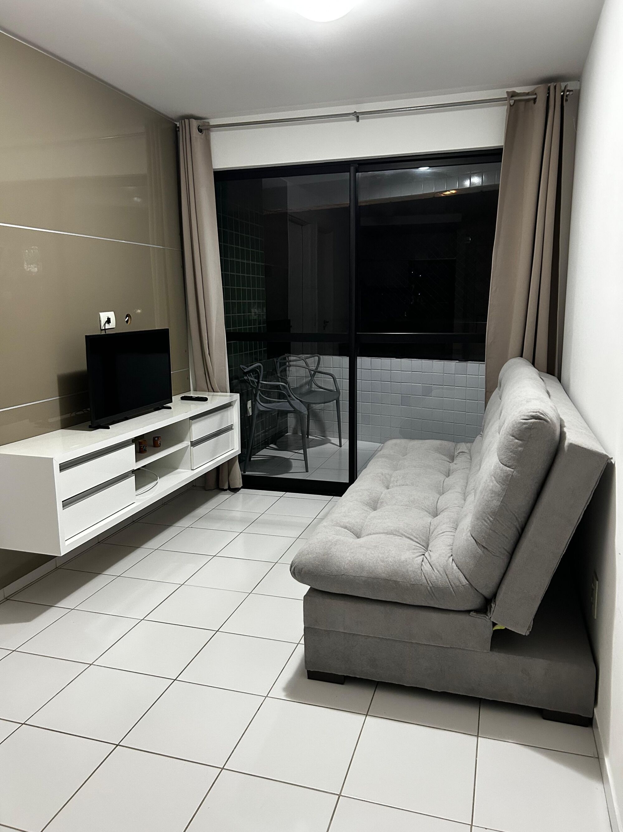Una sala de estar moderna con un sofá, televisor y un ventanal corredera que da a un espacio al aire libre.