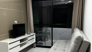 A modern living room with a sofa, TV, and a sliding glass door leading to an outdoor area. - Apartment in the Green Tower Building (Maceió)