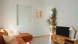 Un soggiorno con un divano, una televisione su un mobile in legno, una lampada e una pianta.