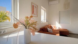 Un soggiorno moderno con un vaso bianco di fiori su un tavolo, un divano marrone e una finestra con persiane.