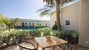 Un tavolo con sedie, una ciotola di croissant e due bicchieri d'acqua in un cortile con piscina e palme.