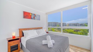 A bedroom with a large window, a bed, a nightstand, and a painting on the wall. - Terraluz Apartment 2D, Wifi & Parking (Papudo)