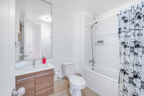 Une salle de bain moderne avec des toilettes blanches, un lavabo avec un miroir et un espace douche.