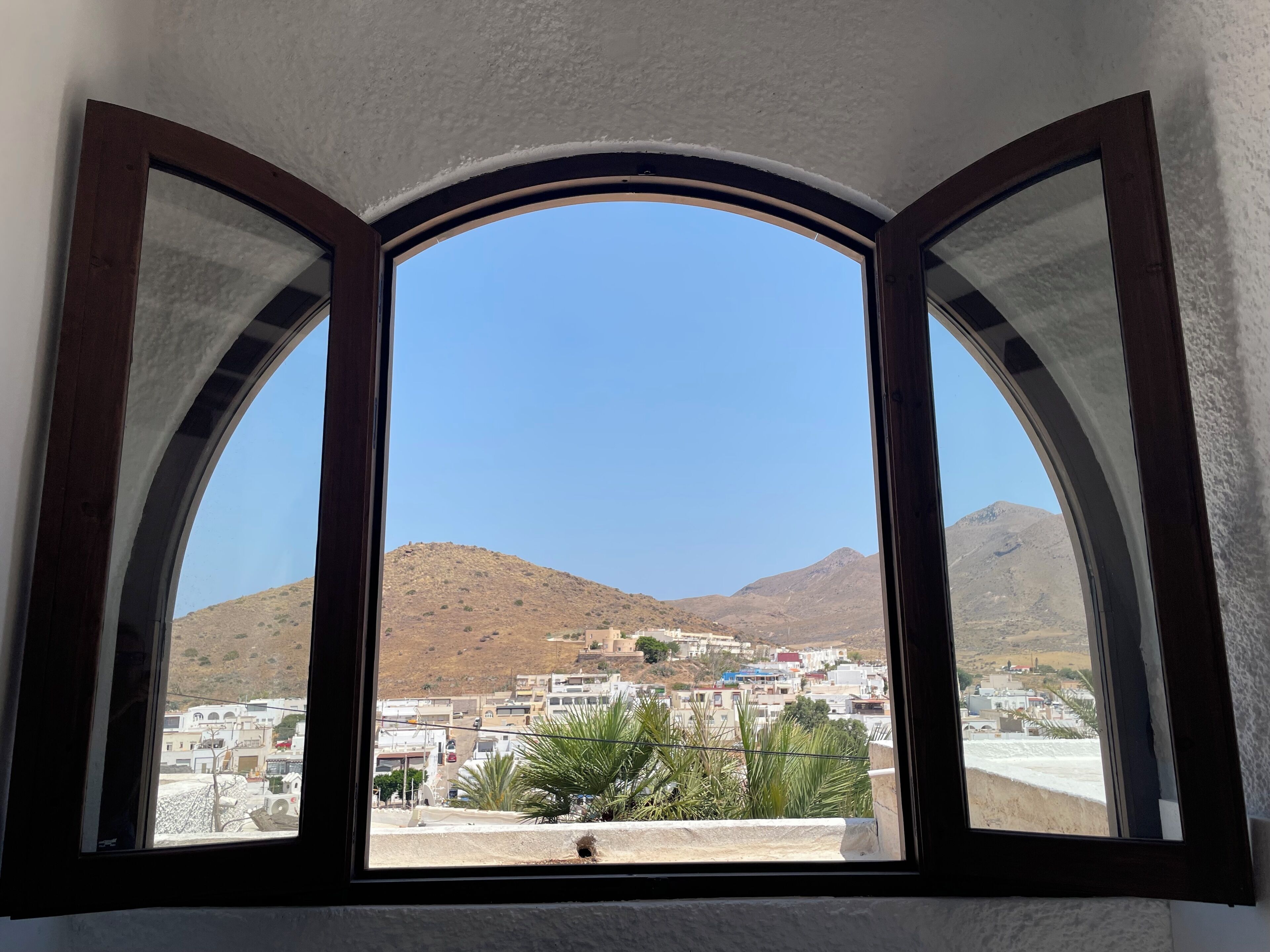 Une fenêtre donnant sur une ville et des montagnes.