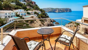 A balcony with a table and chairs, overlooking a coastal area with buildings and cliffs. - Holiday Home 'Ses Gavines en Cala Moragues' with Sea View, Wi-Fi and Air Conditioning (Andratx)