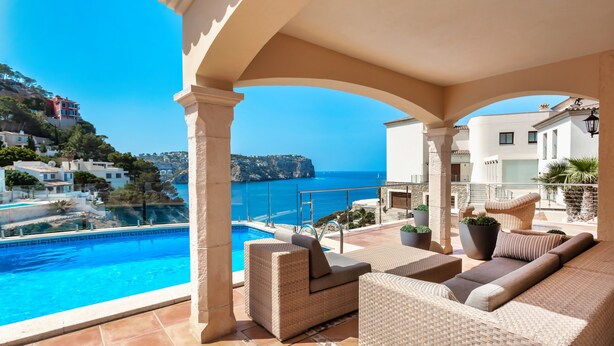 A covered outdoor area with a pool, wicker furniture, and a view of the sea and buildings. - Holiday Home 'Ses Gavines en Cala Moragues' with Sea View, Wi-Fi and Air Conditioning (Andratx)