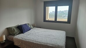 A bedroom with a bed, pillows, a nightstand, a window with a view of buildings, and a lamp. - Luxury apartment with sea view (VC)