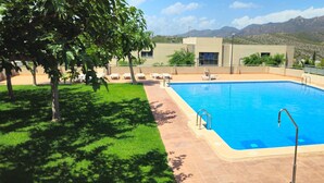 Una piscina con vistas a montañas, un área con césped y un edificio con ventanas.