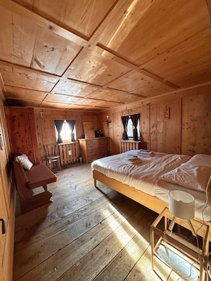 Una habitación de cabaña de madera con una cama, un banco, un escritorio y una ventana.