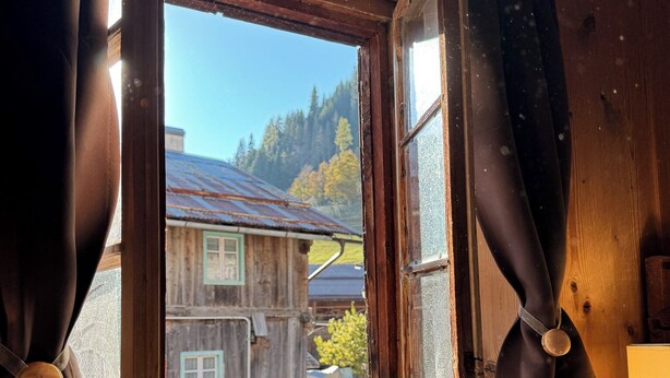 A wooden cabin with a window, curtains, and a view of a house and trees. - Chalet from 1792, authentic alpine soul full of tradition and history without filters (Andraz)