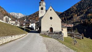 A church with a clock tower, a stone wall, and a road leading to it. - Chalet from 1792, authentic alpine soul full of tradition and history without filters (Andraz)