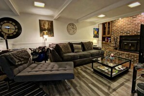 A living room with a sofa, armchair, coffee table, fireplace, and a clock on the wall.