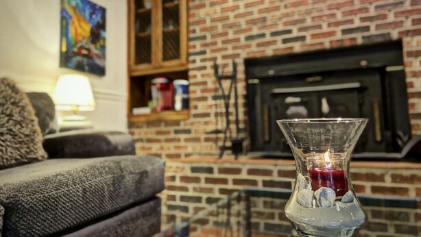 A living room with a brick fireplace, a glass vase with a candle, and a sofa.