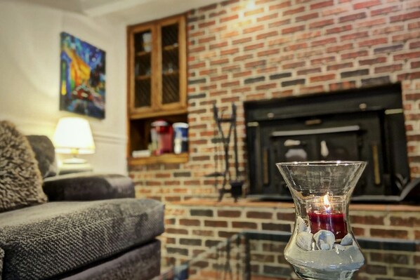 A living room with a brick fireplace, a glass vase with a candle, and a sofa.