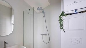 Un baño moderno con cabina de ducha de vidrio, un lavabo blanco y un equipo de aire acondicionado instalado en la pared.
