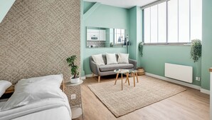 Un dormitorio moderno con una cama, un sofá gris, una mesita y un ventanal grande.