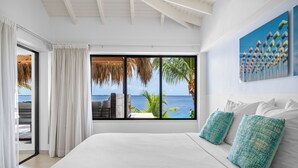 Un dormitorio con una cama grande, vista al océano y un entorno tropical.