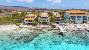 Una propiedad frente a la playa con varios edificios, piscina y aguas turquesas cristalinas.