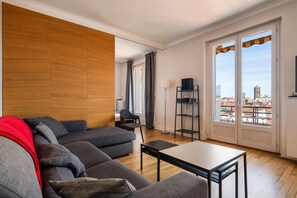 Uma sala de estar moderna com um sofá, uma mesa de centro e vista para a cidade através de amplas janelas.