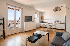 En modern lägenhet med vardagsrum, matplats, kök och stora fönster med utsikt över staden.