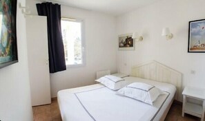 A bedroom with a bed, a nightstand, a window with curtains, and wall-mounted lamps. - Apartment with pools and garden near the beach (La Baule-Escoublac)