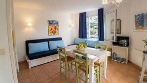 A room with a dining table, chairs, a sofa, a TV, and a window with curtains. - Apartment with pools and garden near the beach (La Baule-Escoublac)