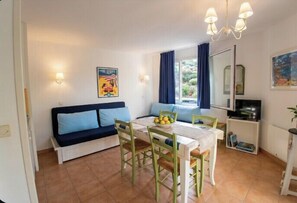 A compact living space with a dining table, chairs, a sofa, a TV, and a window with curtains. - Apartment with pools and garden near the beach (La Baule-Escoublac)