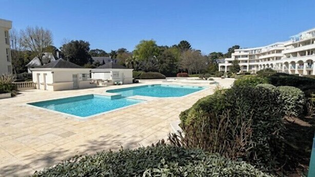 A pool area with two rectangular pools, surrounded by a paved deck and landscaped with bushes and trees. - Apartment with pools and garden near the beach (La Baule-Escoublac)