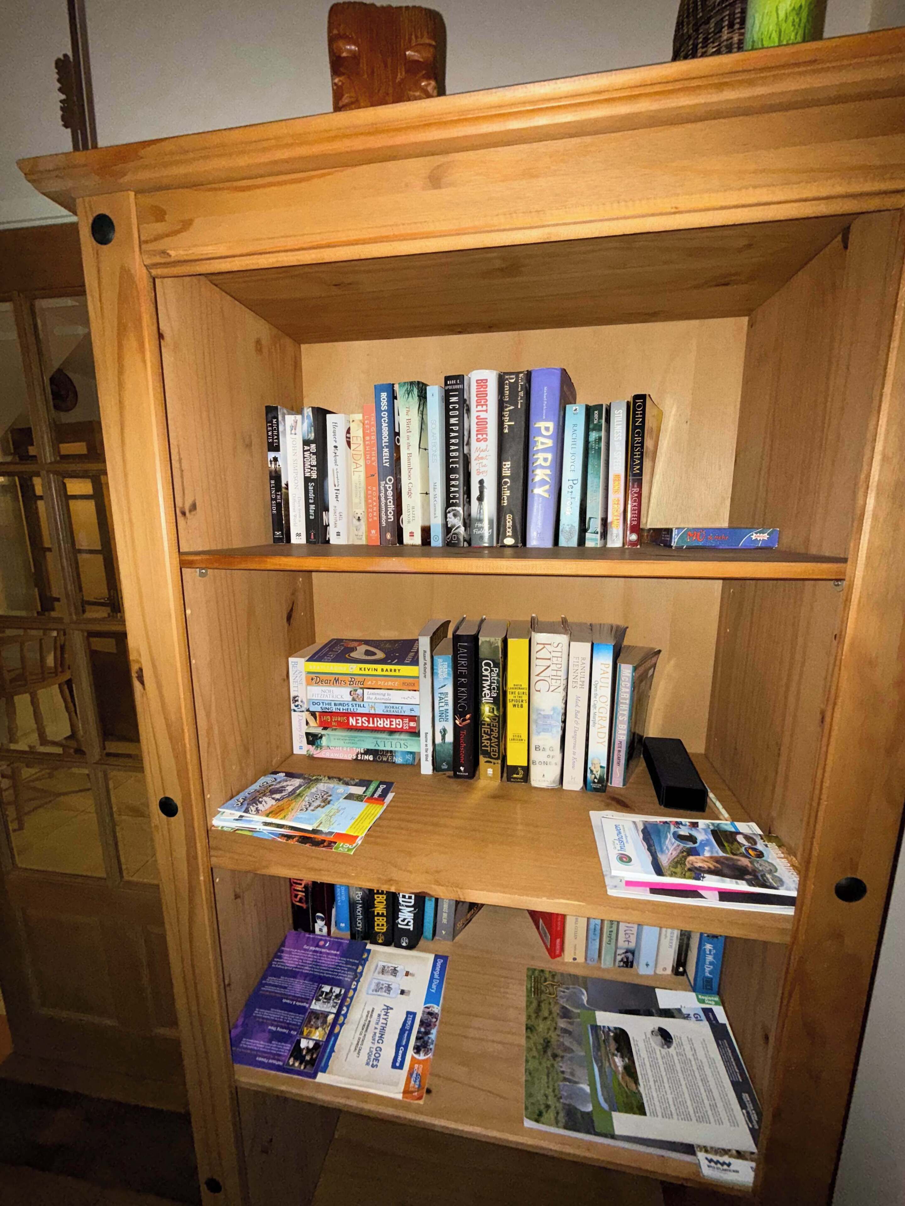A wooden bookshelf with multiple shelves filled with books and magazines.