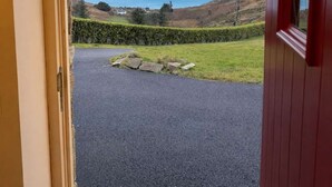 Une porte donnant sur un espace pavé, d’où l’on peut admirer la mer et les collines.