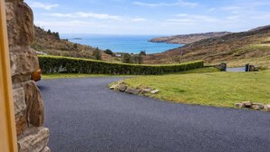 Une route asphaltée qui serpente à travers une zone herbeuse, avec un mur de pierre d’un côté et une vue sur la mer au loin.