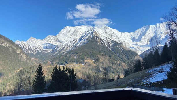 Et bjerglandskab med sneklædte toppe, en skovfyldt dal og en bygning med balkon.