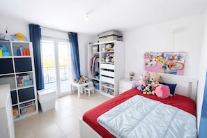 Ein Schlafzimmer mit Bett, Kleiderschrank, Schreibtisch und einem Fenster mit Vorhängen.
