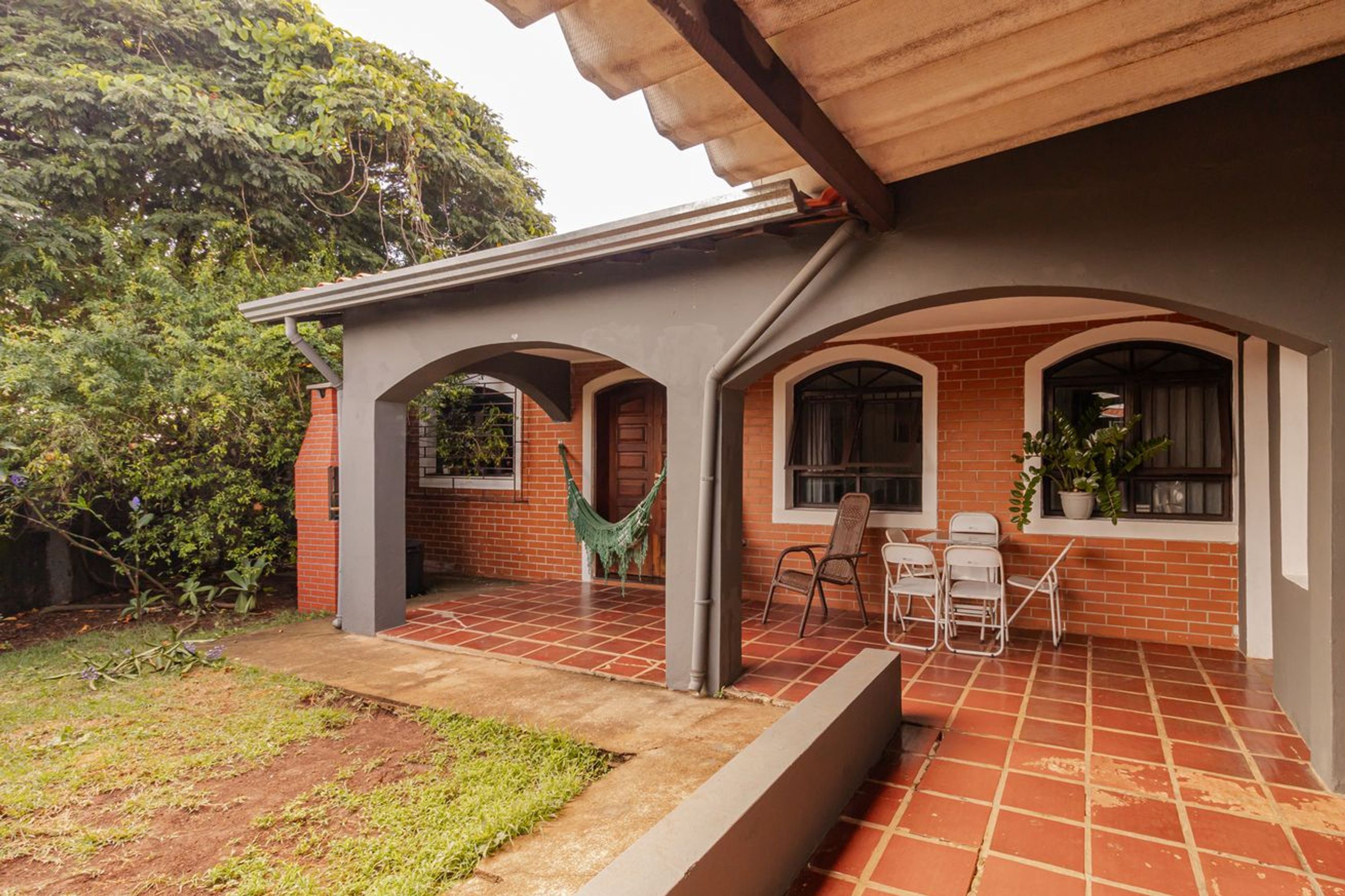 A covered patio with a brick wall, a hammock, and a seating area with chairs.